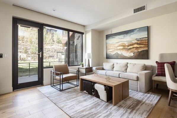 Bright open living space with large picture window and glass patio door for plenty of natural light, living room with full sized white fabric couch and brown leather and black metal accent chair