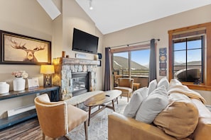The living area features a gas fireplace, mounted flat-screen TV, and access to the private balcony.
