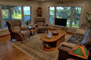Living room with windows looking out at lush greenery and lake.