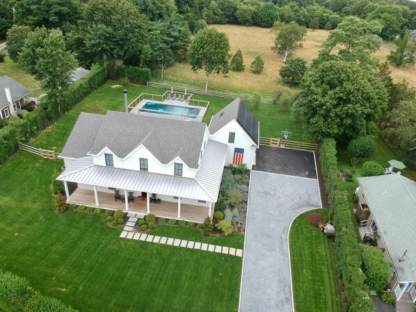 Drone view of property, fenced gunite pool and beautiful field beyond