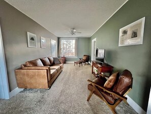 Living room with a 3-4 person couch, two chairs, and two ottomans. TV as well. 