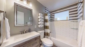 Modern bathroom with a stylish vanity, neatly rolled towels, and a bathtub with striped accent tiles, creating a clean and inviting space.