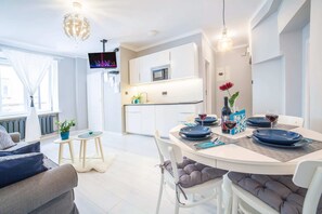 Living room with a sofa bed, TV and kitchenette with dining area.