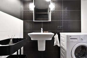 Bathroom with a shower, washing machine, sink with mirror and toilet.