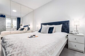 A sophisticated bedroom with a large bed, gray upholstered headboard, and white bedding, paired with a bedside table and stylish lamps for a warm, inviting atmosphere.