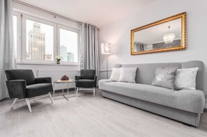 A comfortable living room with a large gray sofa, a glass coffee table, and a large window that lets in plenty of natural light, creating a calm and stylish environment.