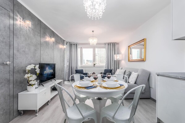 A luxurious dining room with a crystal chandelier, a round dining table set for four with elegant white chairs, and a mirror that adds a sense of space and brightness.