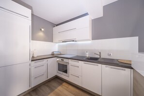 A contemporary kitchen with sleek white cabinets, modern appliances, and a wooden floor, blending functionality with style.