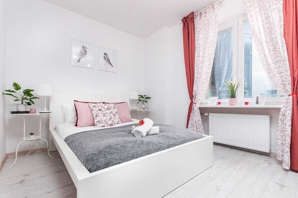 Bright and cozy bedroom with a double bed with gray and yellow and decorative pillows that match the color of the curtains hanging in the window.