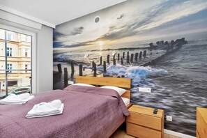 The bedroom includes a cozy bed covered with a purple throw and a stunning mural of a beach scene on the wall, creating a relaxing atmosphere.