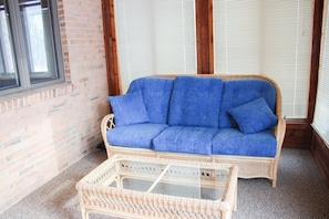 Relax in the enclosed front porch, equipped with sofa, chair, & reading table.