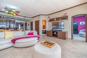 The living room with TV, sofa, and kitchen beyond