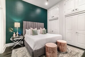 Spacious master bedroom with king-size bed, ensuite bathroom, and designer built-in closets. The room includes a lamp, hangers, luggage racks, alarm clock, white noise machine, and a 50'' Samsung Smart 4K TV for streaming and DIRECTV Entertainment.