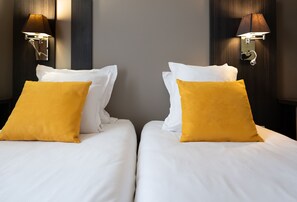 A close-up of the inviting beds emphasizes plush white linens and soft yellow pillows, set against a contemporary backdrop, ensuring a restful atmosphere for guests.