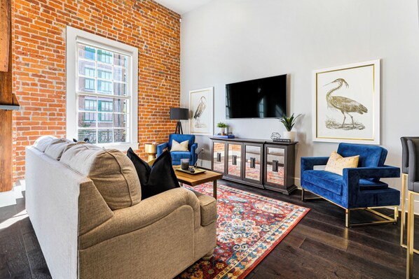 Open-concept living, kitchen, and dining area with ample seating. 65” Samsung Smart 4K TV with streaming and DIRECTV Entertainment. Sofa converts to a queen sleeper. Dining table seats four. Enjoy plenty of natural light!