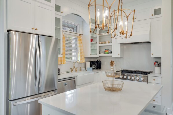 - White quartz island offers space to prep, serve, or gather for quick bites and conversation - Brass pendant lighting adds warmth and style to the bright kitchen layout - Stainless steel appliances pair with shaker cabinets for classic charm