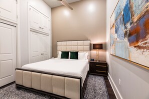 Spacious guest bedroom with a king-size bed and designer built-in closet. Features nightstand, lamp, hangers, luggage rack, alarm clock, white noise machine, and a 50'' Samsung Smart 4K TV with streaming and DIRECTV Entertainment.