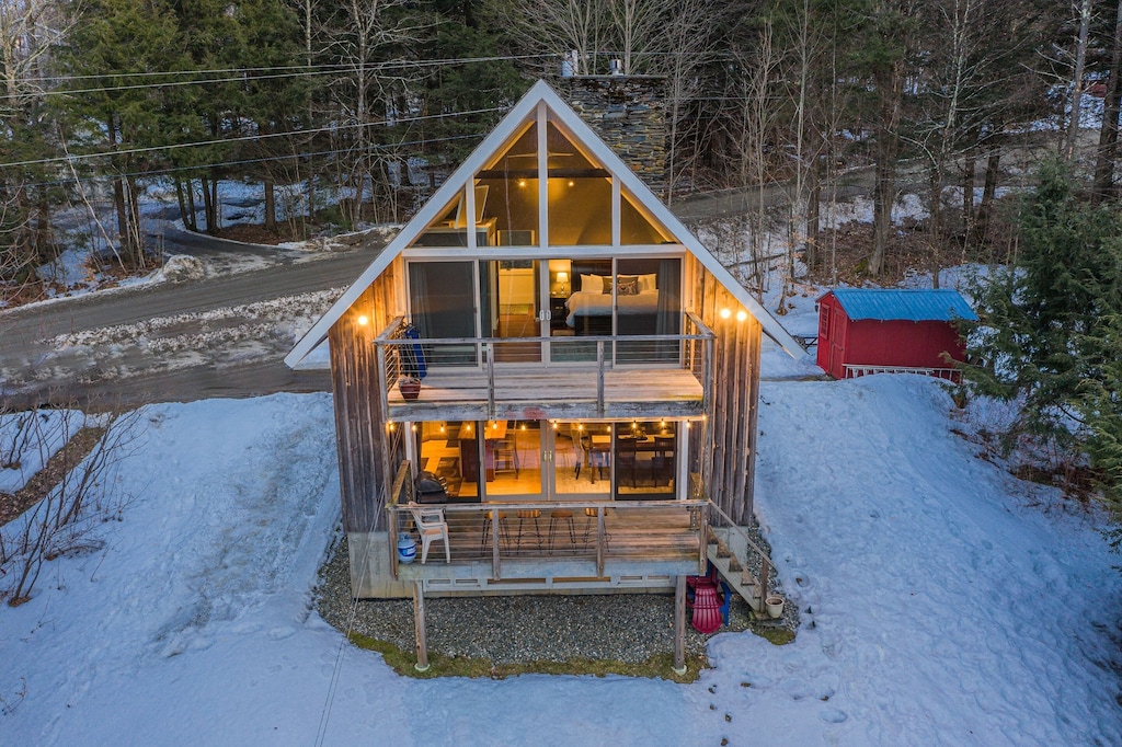 An A frame Stowe ski chalet at dusk is illuminated from within as snow lays on the ground around it