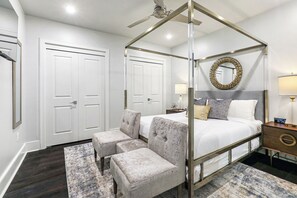 Spacious guest bedroom with queen-size bed, ensuite bathroom, and designer built-in closet. Features nightstands, lamps, hangers, luggage rack, alarm clock, white noise machine, and a 43" Samsung Smart 4K TV with streaming and DIRECTV Entertainment.