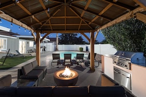 Covered gazebo with bistro lights, outdoor furnishings, fire-pit, and BBQ.