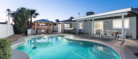 Backyard with large pool, sun loungers, covered patio with 6 person outdoor dining table, and a covered gazebo with bistro lights, outdoor furnishings, fire-pit, and BBQ.