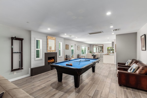 Open-concept living space overlooking the kitchen and dining area featuring a pool table for friendly competition, and a warm fireplace.