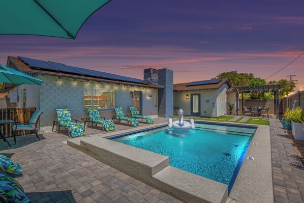 Stunning valley backyard featuring a sparkling blue heated pool with sun loungers, a BBQ grill, and outdoor dining while bistro lights set the mood.
