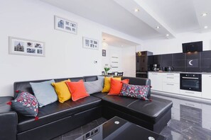 A cozy living room featuring a dark sofa adorned with vibrant throw pillows. The space is accented with subtle decor elements like plants and decorative wall art.