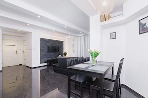 An open-plan area combining the living room and dining space, furnished with a modern table and chairs. Light walls and contrasting dark accents create a minimalist and functional atmosphere.