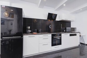 A modern kitchen equipped with glossy dark cabinets, a white countertop, and state-of-the-art appliances. The reflective surfaces amplify the light, making the space feel more expansive.