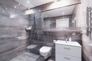 A luxurious bathroom with a walk-in shower. The walls are clad in gray, stone-like tiles, and the elegant fixtures add sophistication to the interior.