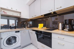 A sleek and modern kitchen with wooden countertops, white cabinetry, and stainless-steel appliances. A washing machine is integrated into the setup, adding practicality.