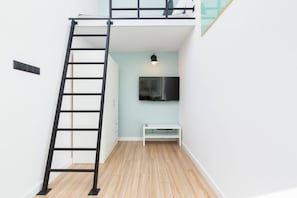  A clean and sleek white loft-style bedroom with a TV and ladder. Ideal for compact spaces.