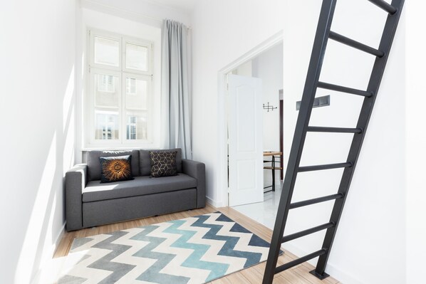 A contemporary, bright living room featuring a black loft ladder, a cozy gray sofa, and a patterned rug. Perfect for small apartments.