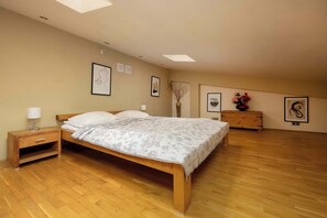 A spacious bedroom with a double bed and minimalist decor beneath a sloped ceiling and skylight.