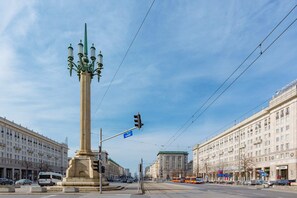 A city center square with a tall column monument, surrounded by historic buildings and tram lines.

