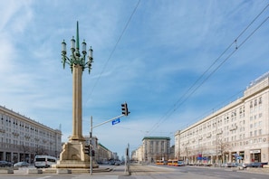 A city center square with a tall column monument, surrounded by historic buildings and tram lines.