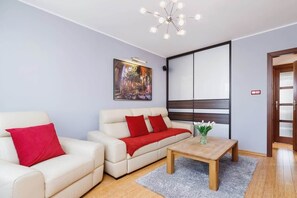 A living room with a beige sectional sofa, red cushions, and a coffee table, set against a bold red accent wall. The space is bright and modern.