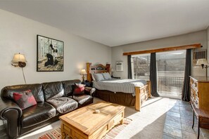 Cozy studio with queen bed, sofa, TV, and outdoor patio view.