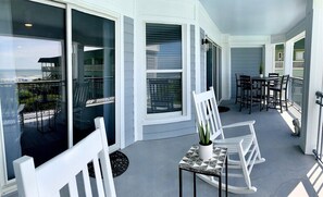 A spacious balcony with outdoor rocking and dining chairs.