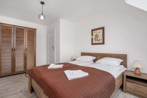 A bright bedroom featuring a large wooden bed with brown bedding, a wardrobe with sliding doors, and an elegant pendant lamp hanging above.