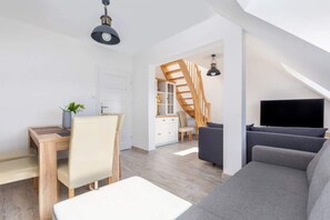 A bright living room with a gray sectional sofa, a wooden table with chairs, and a staircase perfectly integrated into the space.