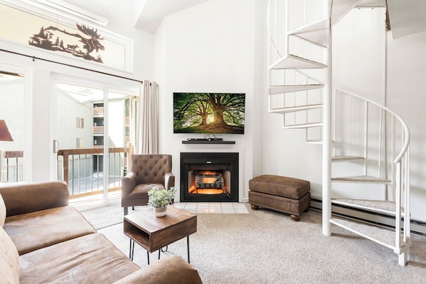 Bright living room with wall mounted flat screen TV and sound bar, spiral staircase leading to the loft