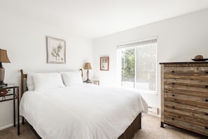 Bright main bedroom with picture window, wooden chest and bedside tables