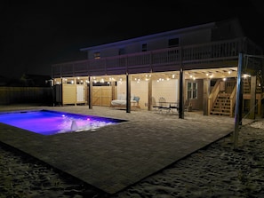 Night view of the back yard with lighted pool and cafe lights under the deck.