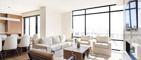 Stunningly bright living room with striking window walls, hardwood floors and large area rug, white couch, two white arm chairs, and leather and black metal accent chair