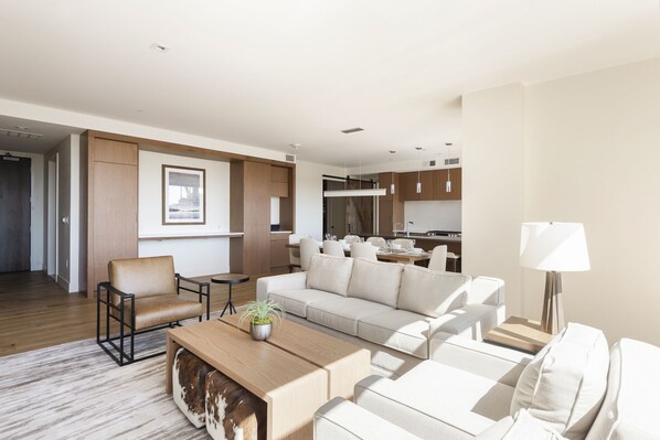 Bright living room with solid wood coffee table, white couch and leather accent chair, with dining and kitchen in the background