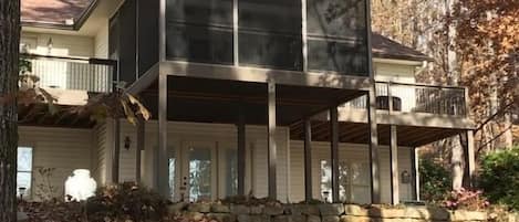 Back of house with large screened porch & 2 decks looking up from water. 