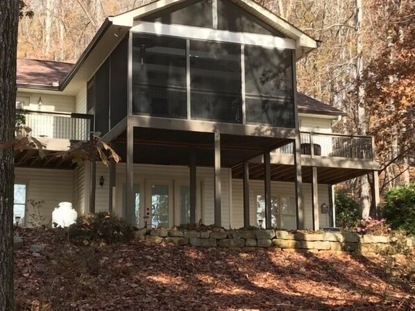 Back of house with large screened porch & 2 decks looking up from water. 