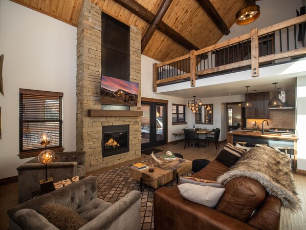 Living area with 25 foot tall fireplace and 50 inch smart TV looking into the kitchen